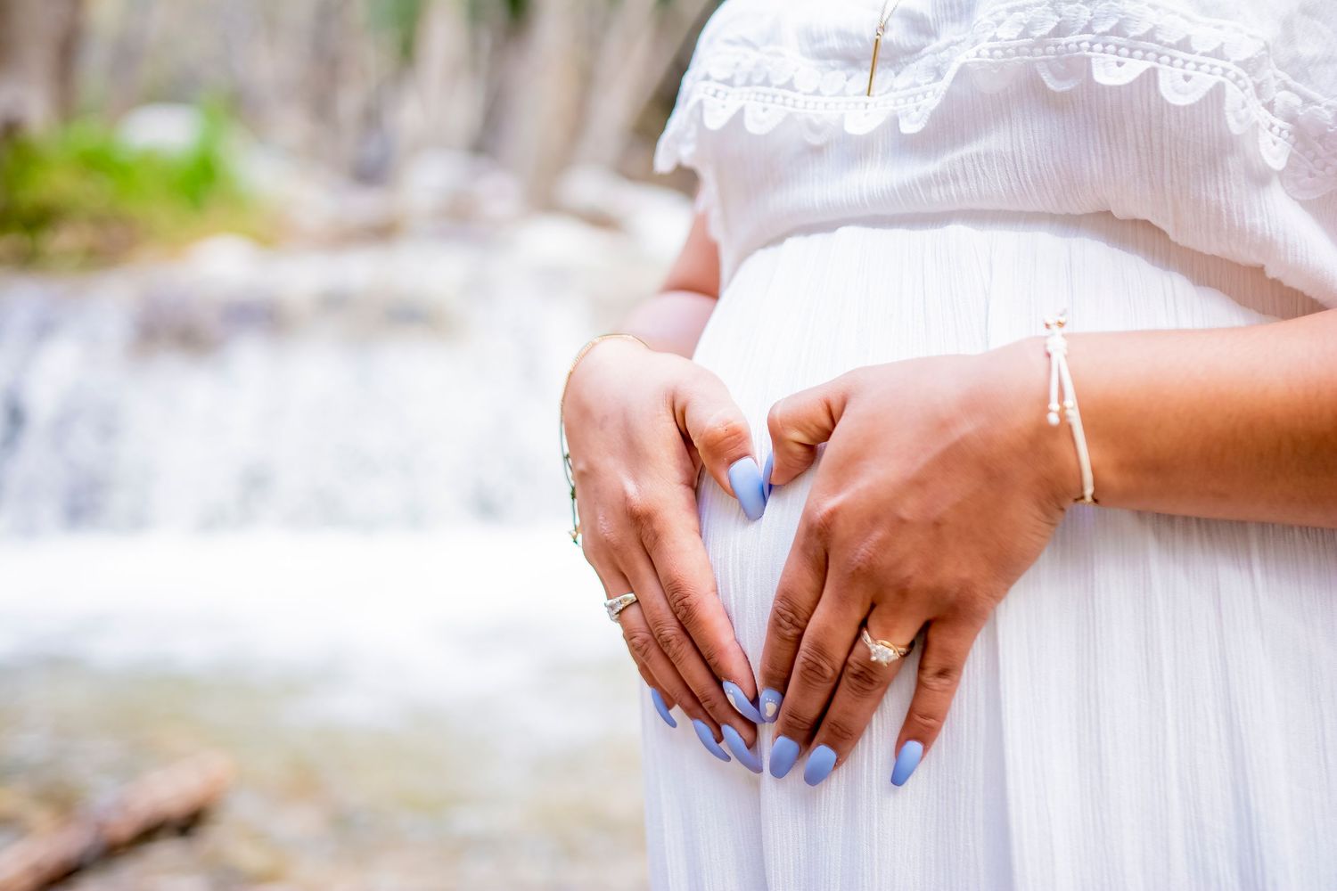 Hands gently cradling a pregnant belly in white lace dress.