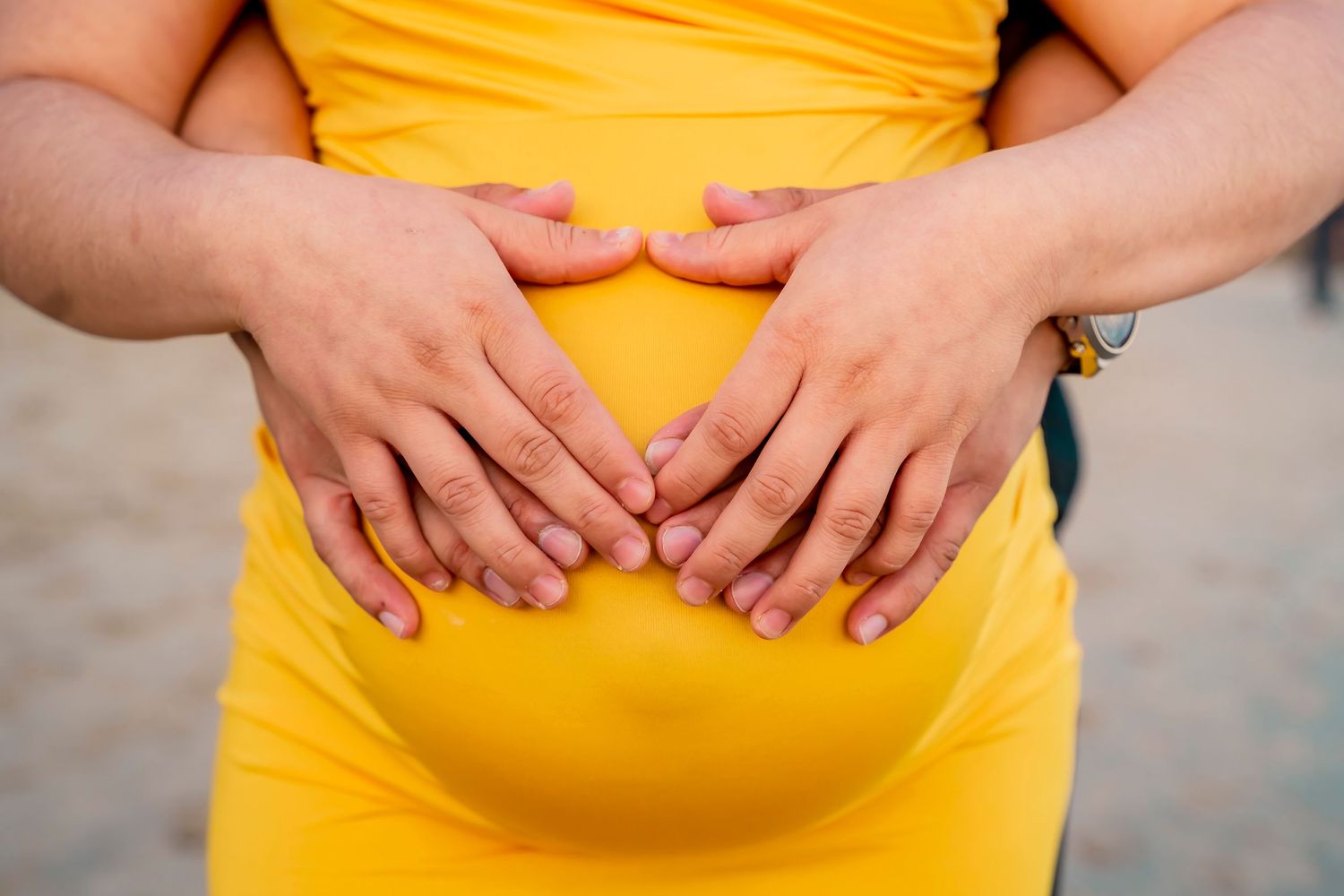 Hands form a heart shape over a yellow maternity dress.