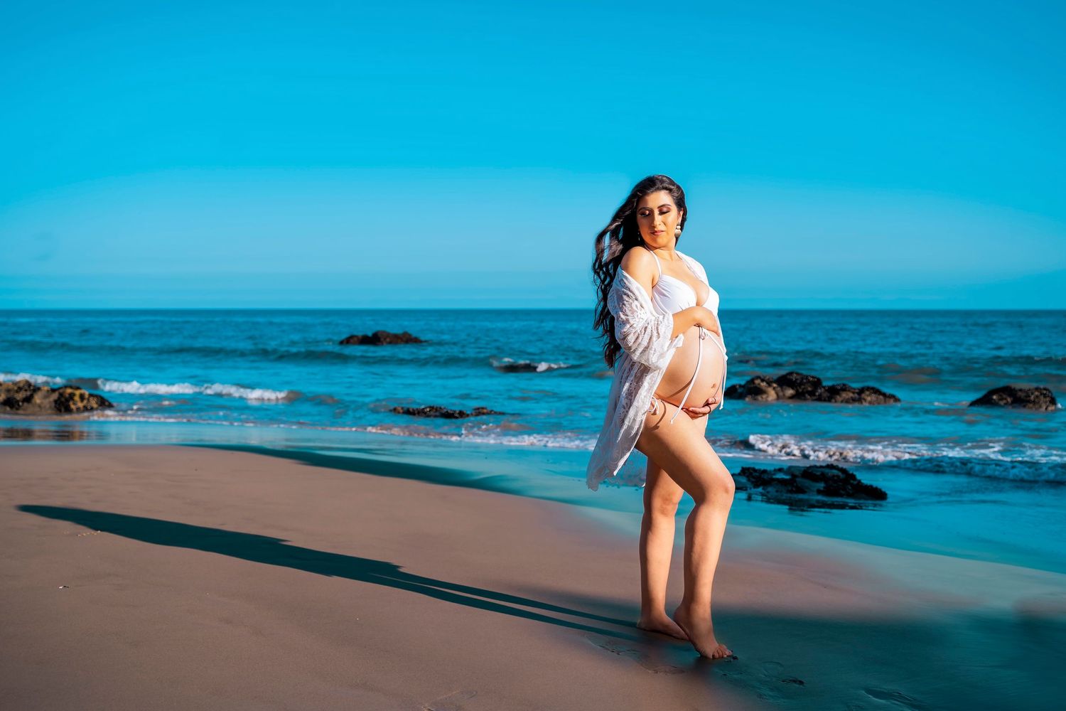 A dreamy beach photoshoot with soft lighting and ocean rocks in the background.