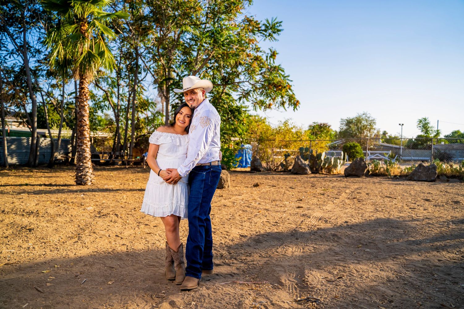Outdoor maternity photoshoot with couple in rustic setting with palm trees.
