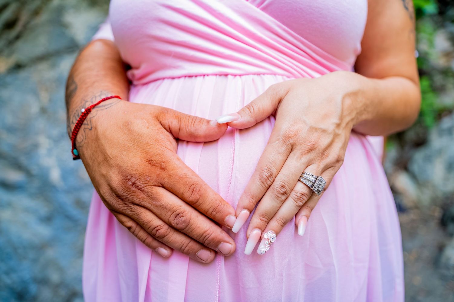 Close-up of hands forming heart shape on pink maternity dress.