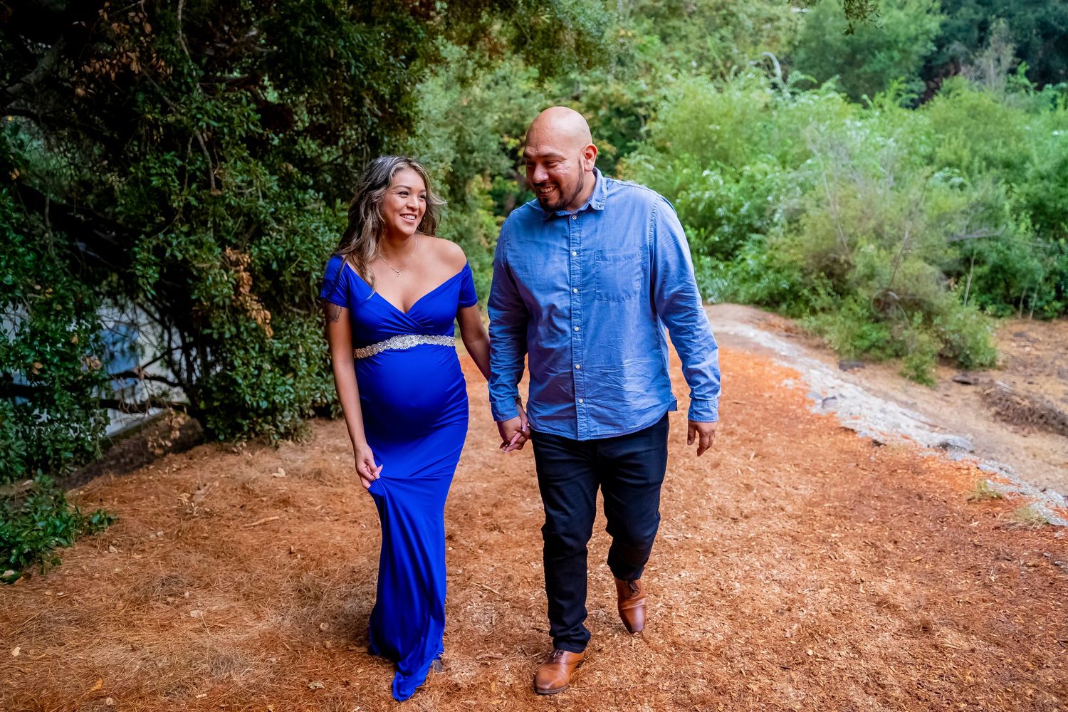 Couple walking hand in hand on dirt path during maternity photoshoot.