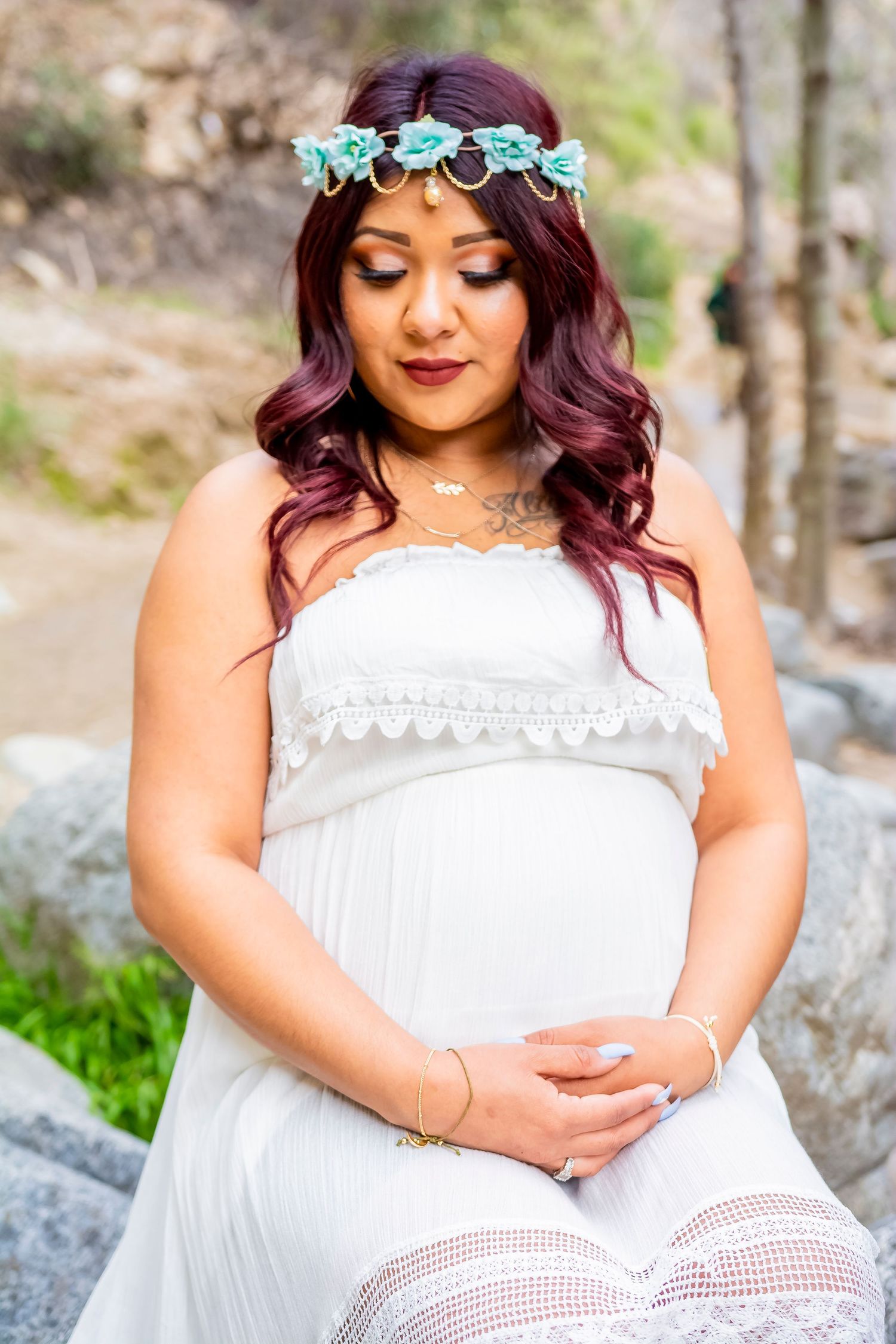 Woman in white lace dress wearing floral crown poses in outdoor mountain setting.