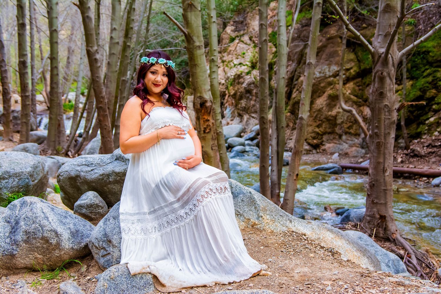 Maternity photo shoot by a mountain stream with subject in flowing white dress.