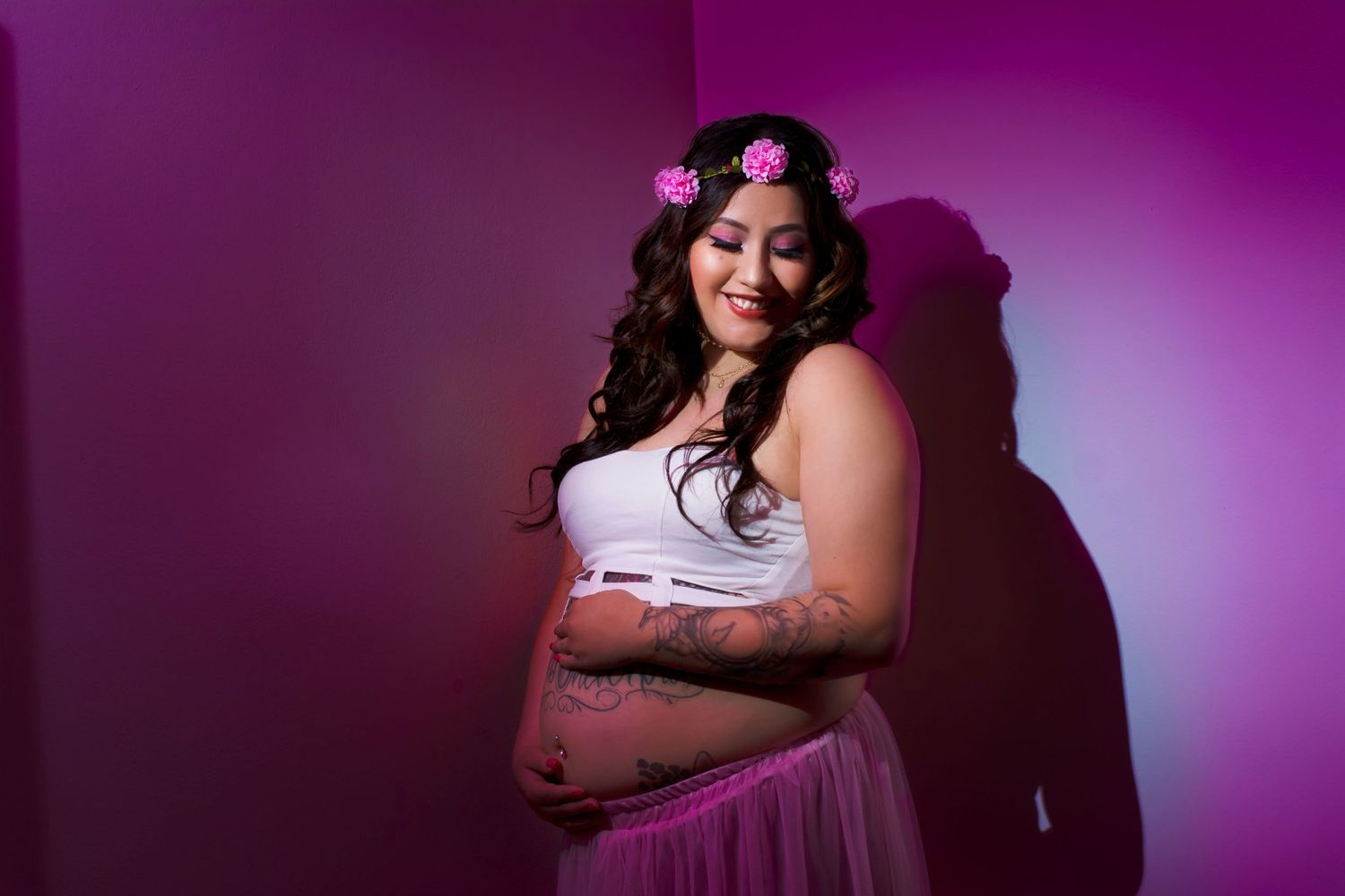 A maternity portrait with purple lighting and floral hair accessories.
