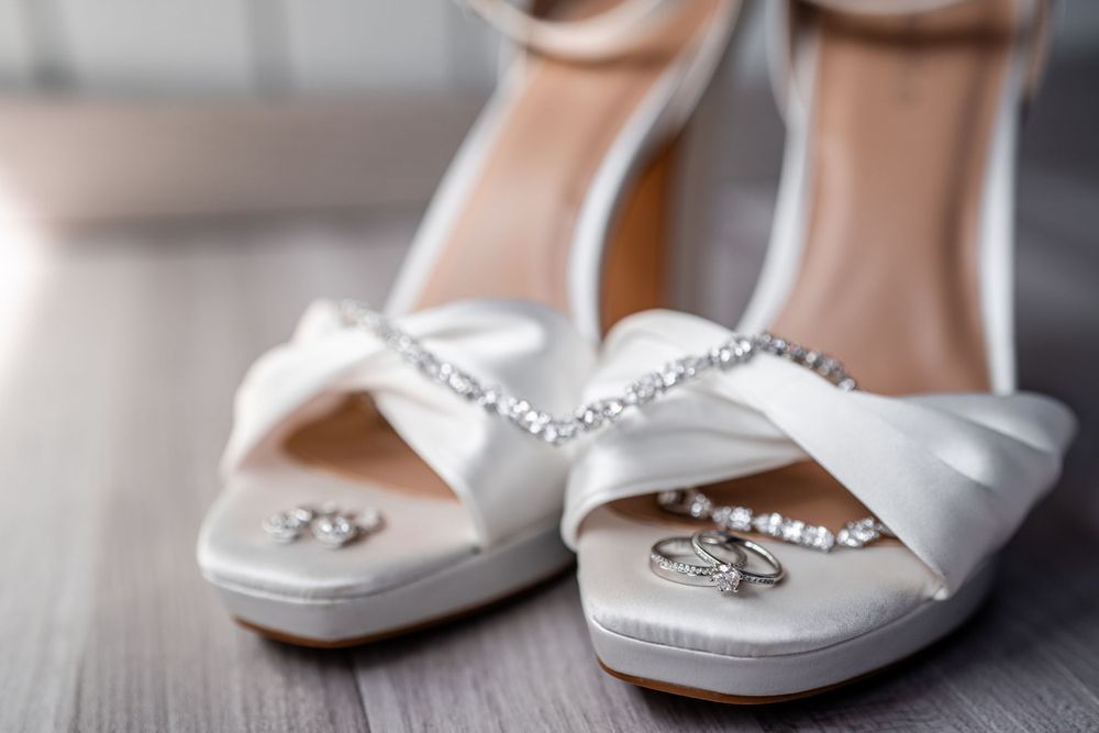 Elegant white bridal shoes with crystal embellishments on wooden floor.