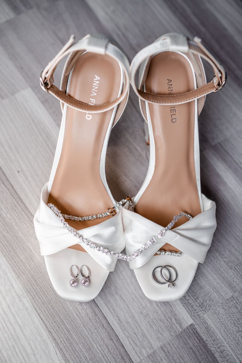 White satin wedding sandals with rhinestone details and wedding rings displayed.