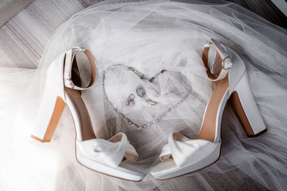 White wedding heels rest on delicate tulle fabric with a heart shape design in the background.