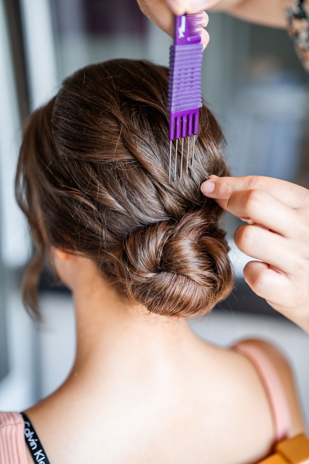 Hairstylist using purple comb to create elegant updo hairstyle.
