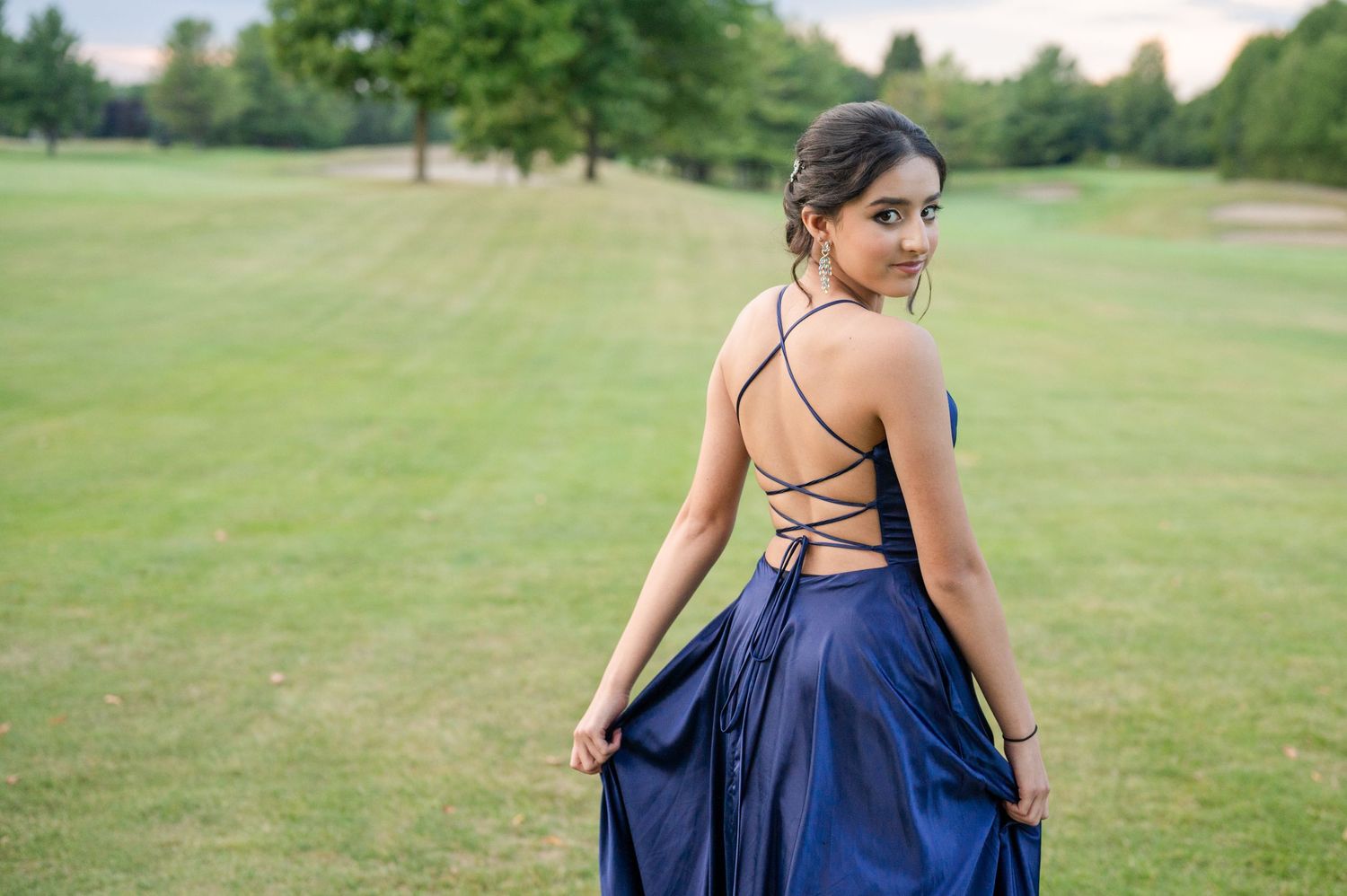 Navy formal dress with strappy back detail photographed in park setting.