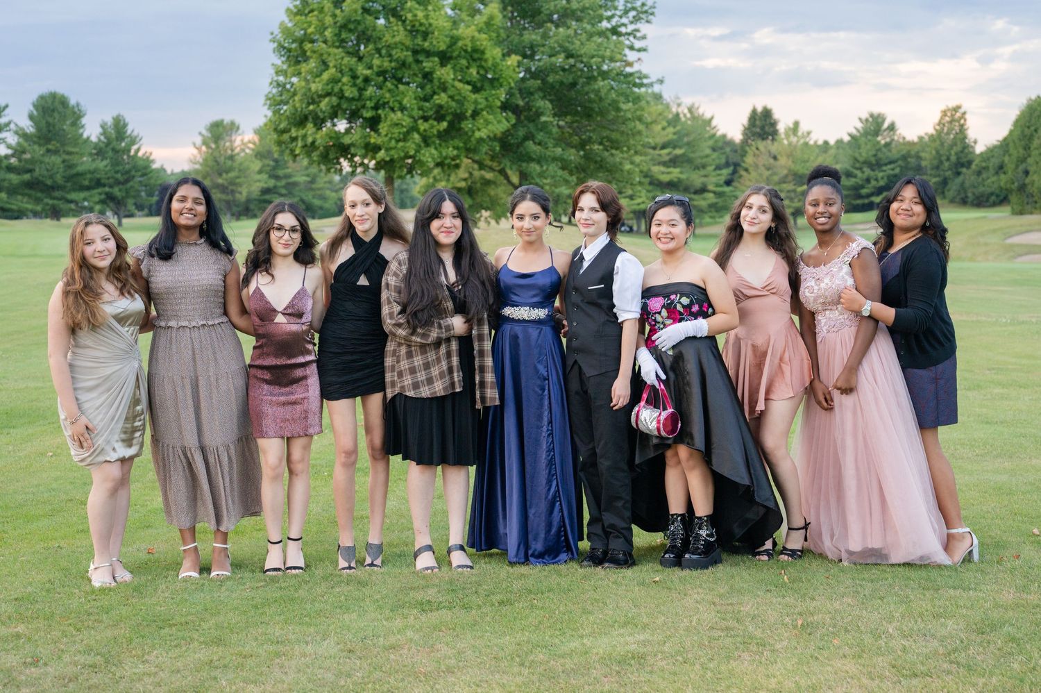 Group photo of formal attire on grassy field during sunset.