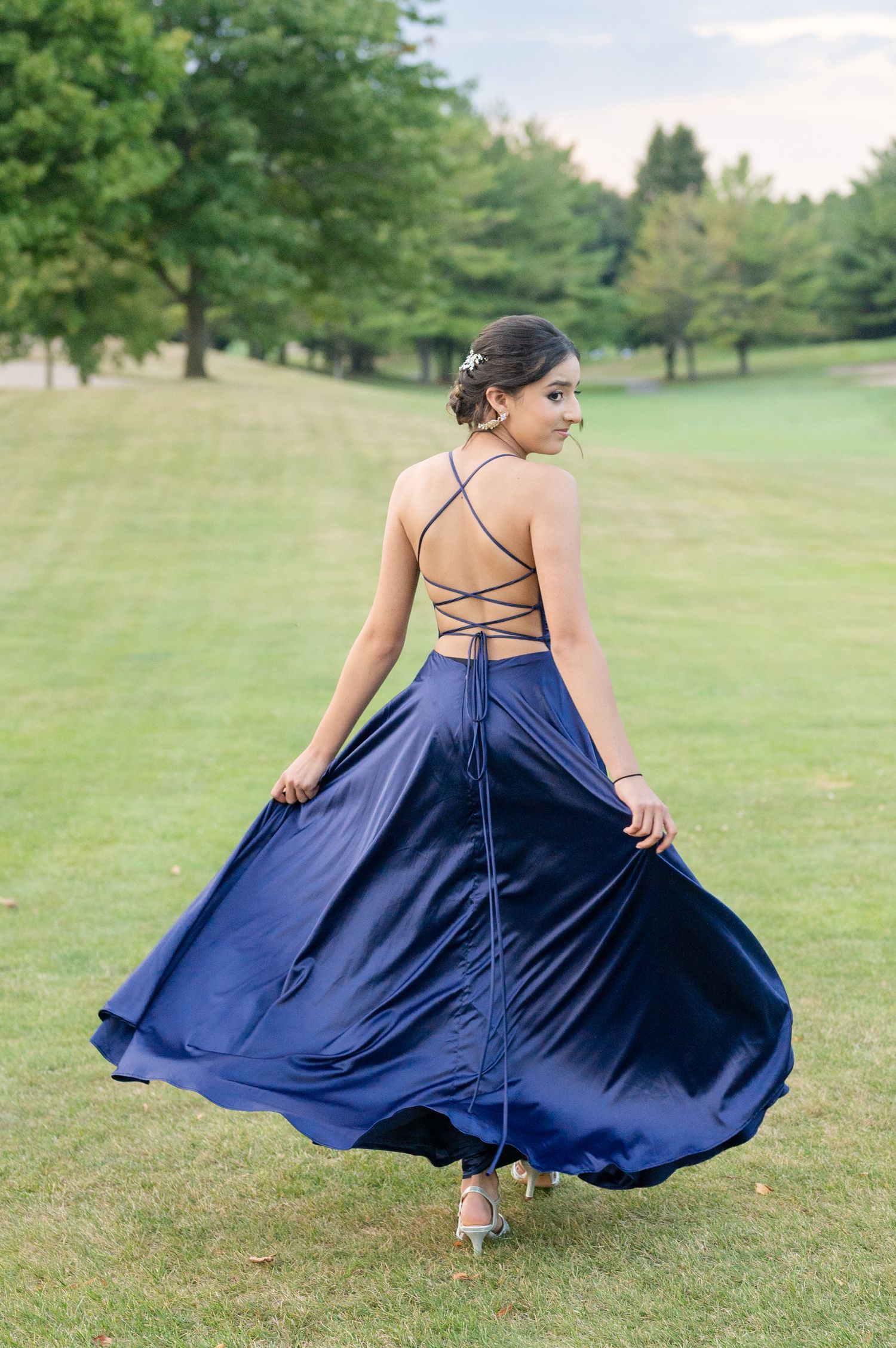 Navy blue gown with laced back twirling on grass field.