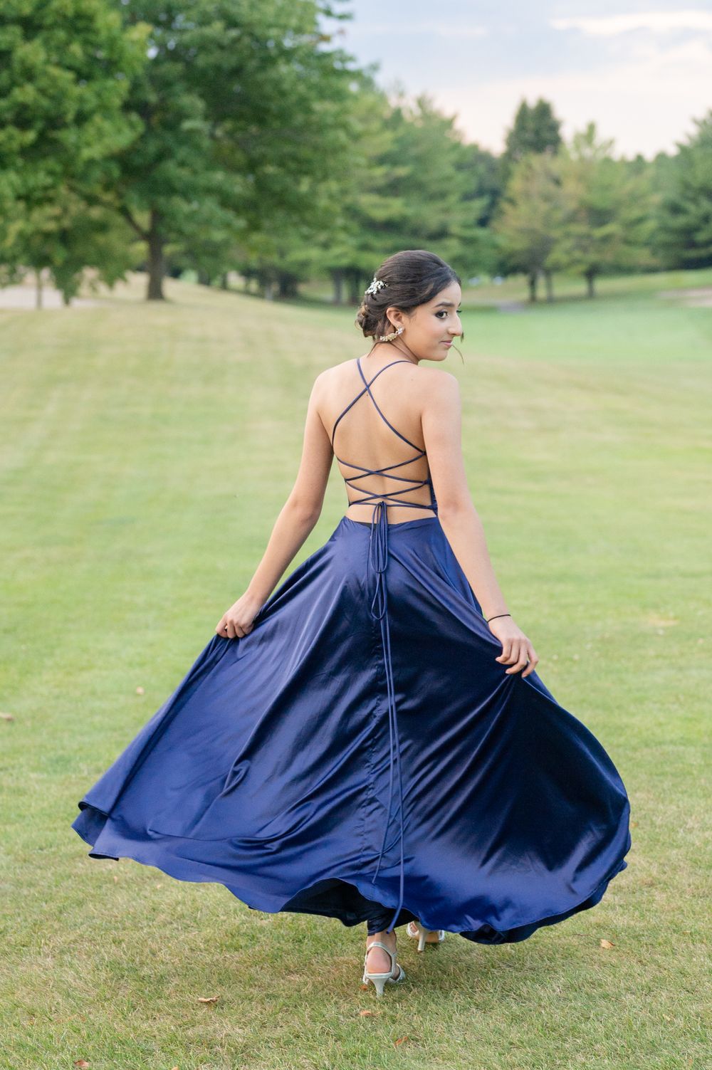 Navy blue gown with laced back twirling on grass field.