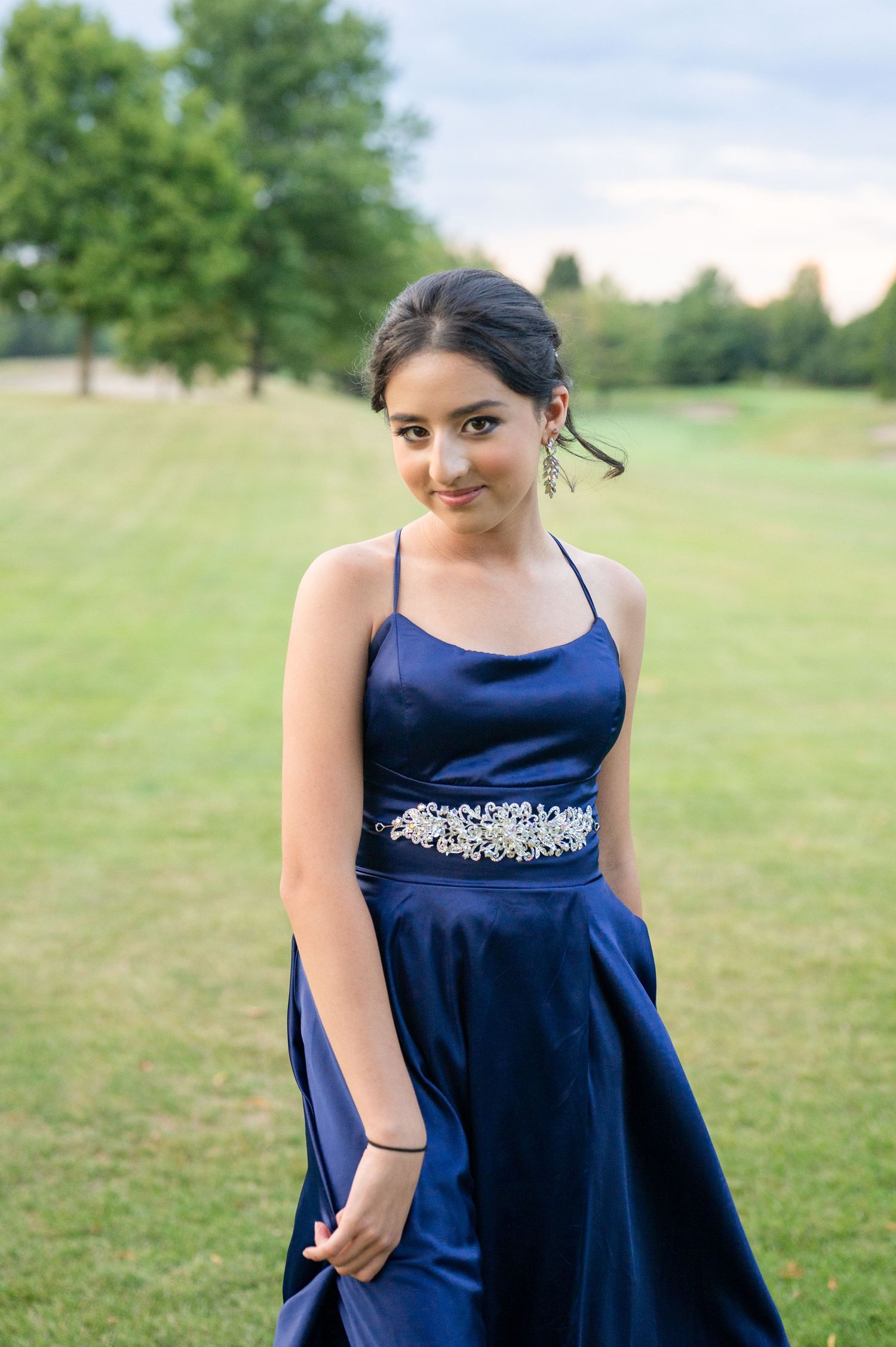 Navy satin formal dress with crystal belt detail in outdoor garden setting.