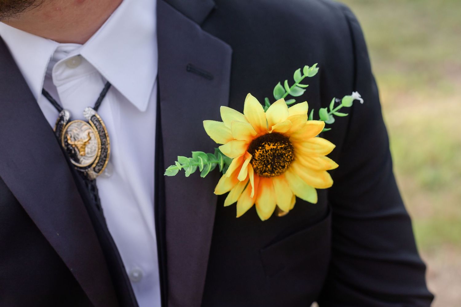 Close-up of sunflower boutonnieres on dark suits at outdoor wedding.