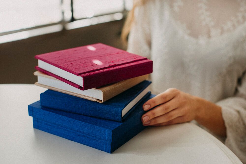 Stack of blue and burgundy velvet photo albums on white table.