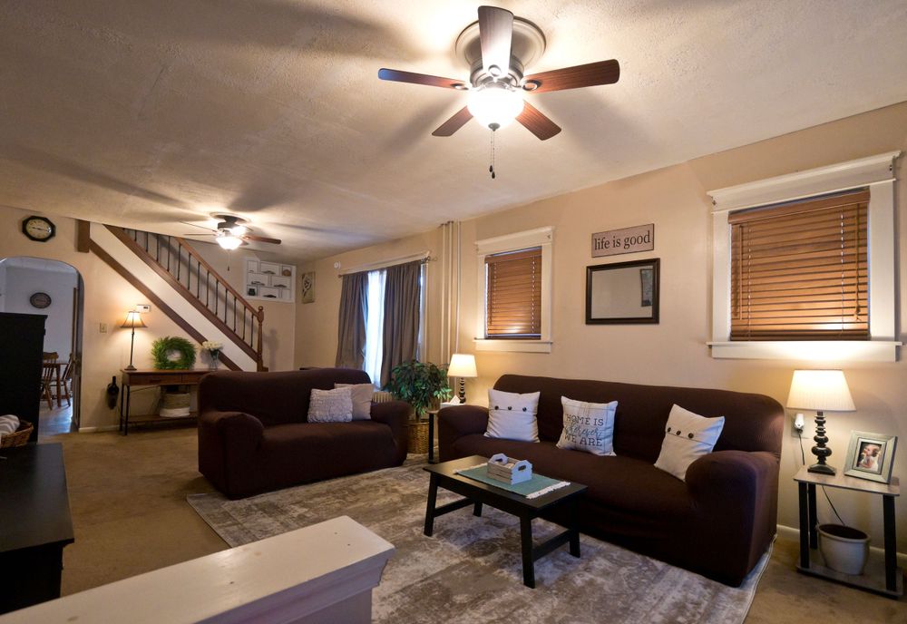 Cozy living area with brown leather couches, area rug, and staircase in background.