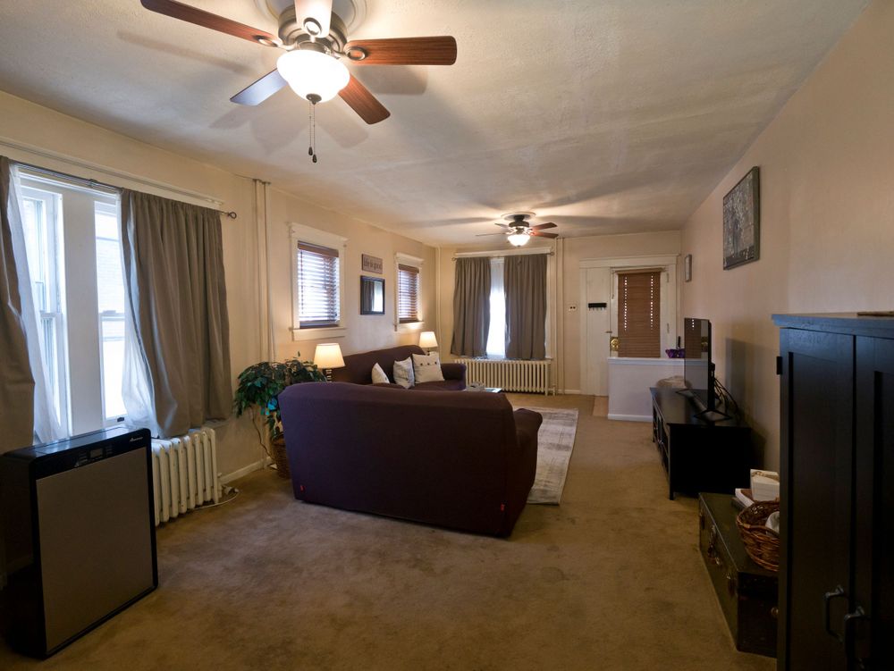 Large living room with brown sectional sofa, ceiling fan, and multiple windows.
