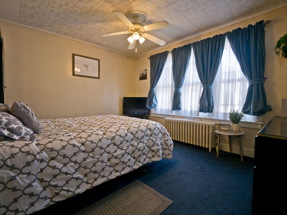 Cozy bedroom with navy curtains, patterned bedding, and a ceiling fan features natural light from large windows.