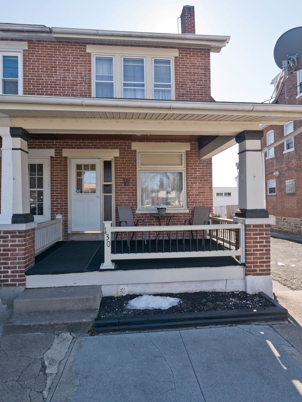 Traditional brick house with white-trimmed windows and covered front porch featuring square columns.