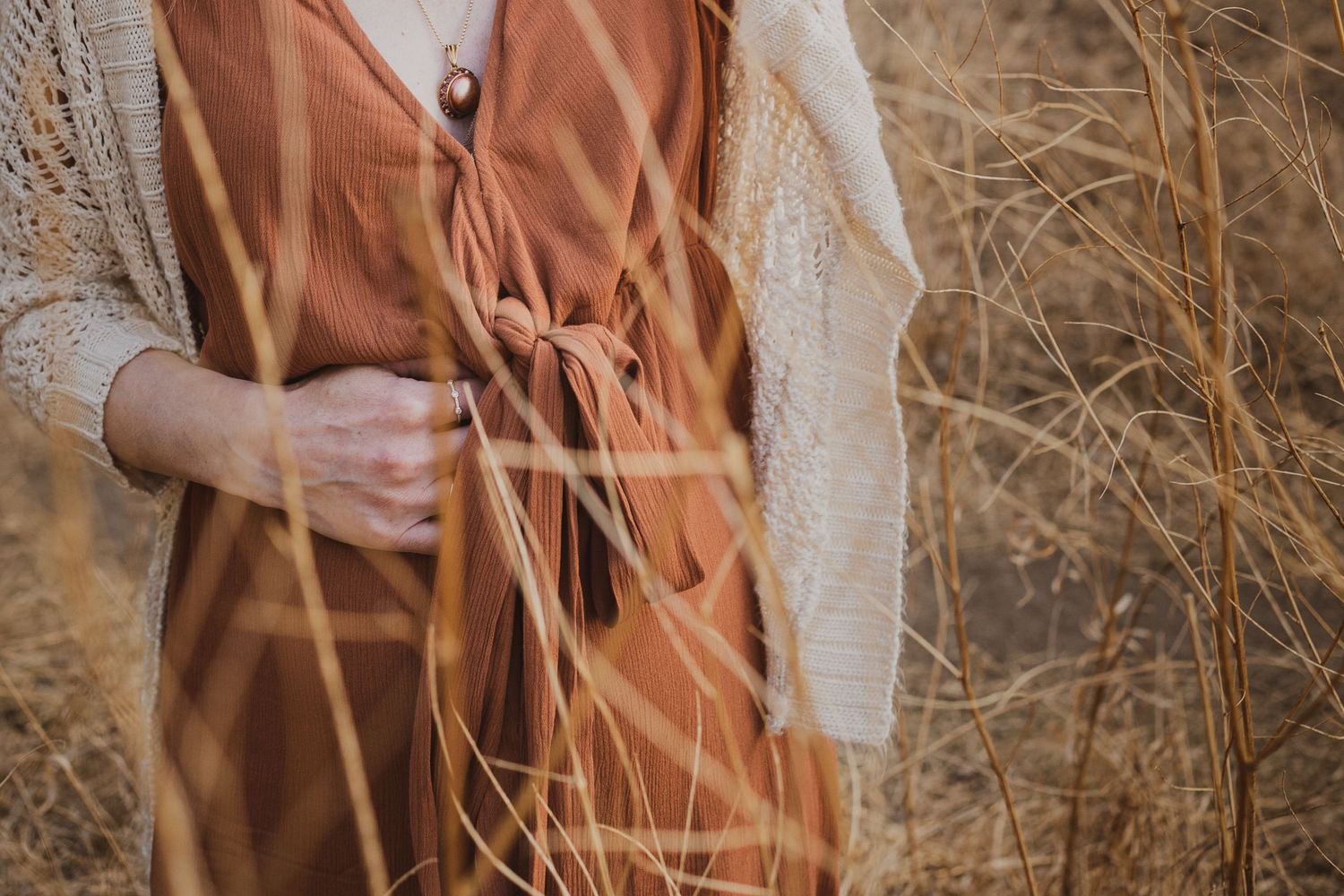 Detail shot of rust-colored maternity dress with cream knit sweater against fall foliage.