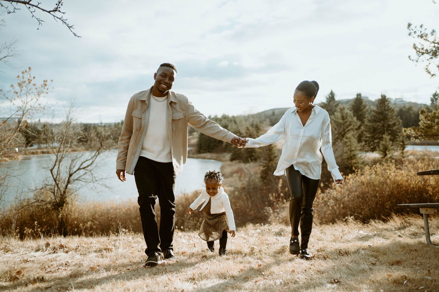A family holds hands while walking together on a path overlooking a serene lake.