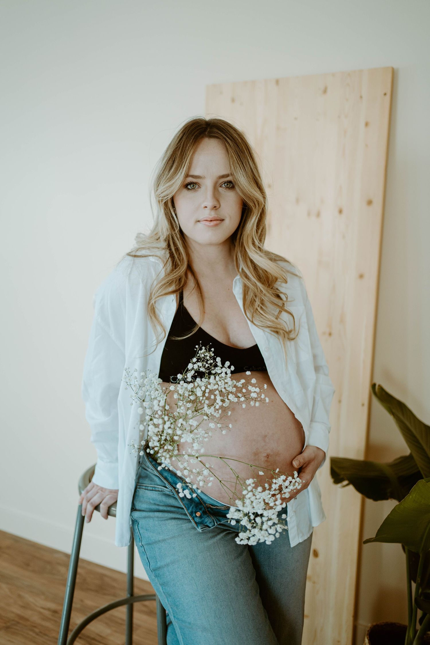 Maternity photo with delicate baby's breath flowers held against a pregnant belly in casual attire.