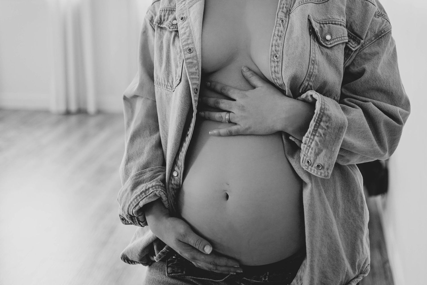 Black and white close-up of pregnant belly with denim jacket.