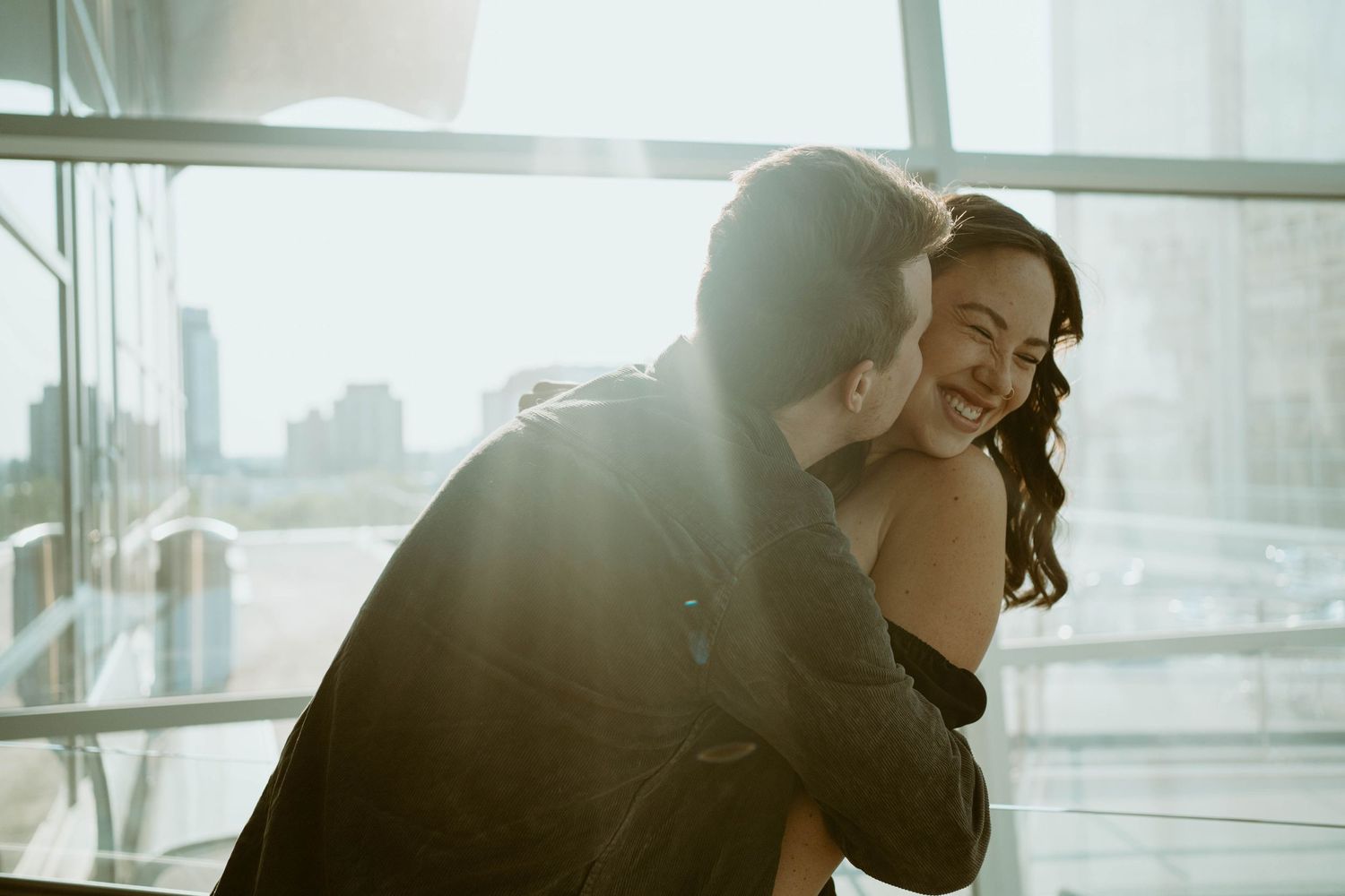 A romantic embrace captured in soft sunlight against a city backdrop.