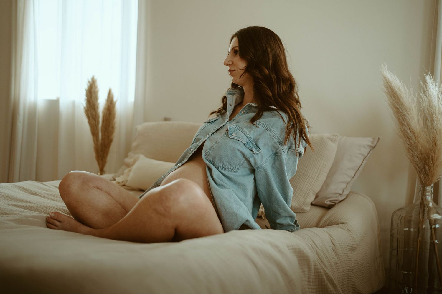 Maternity portrait in soft lighting with pampas grass decor and cozy bedroom setting.