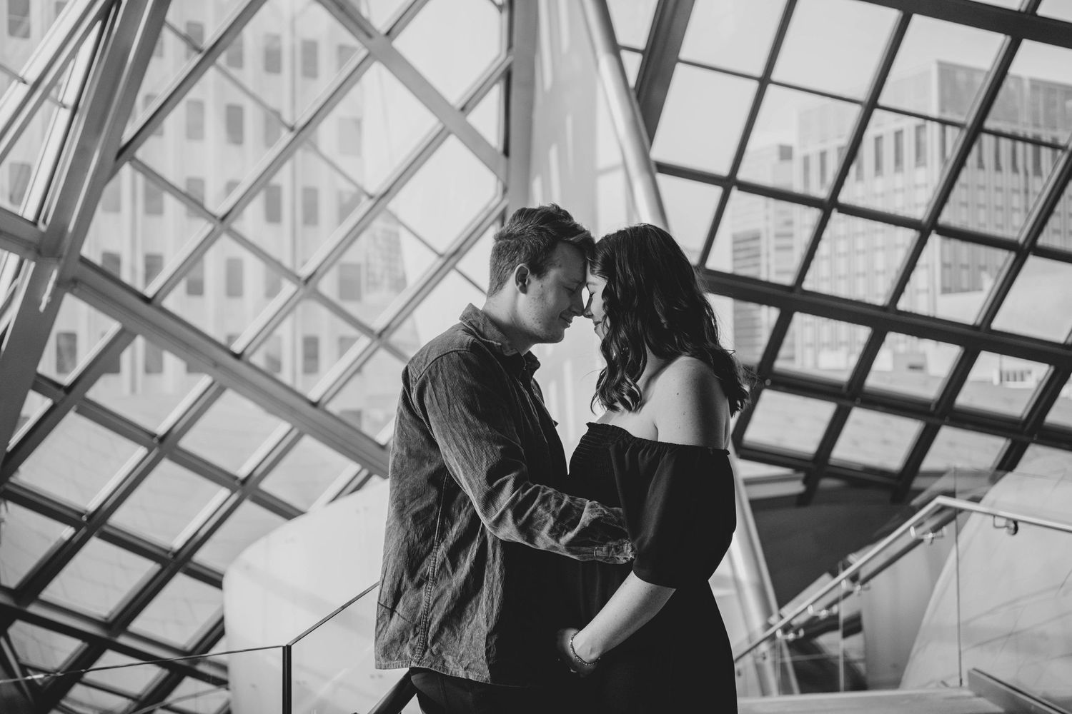 A romantic black and white photo of a couple embracing under a geometric glass ceiling.