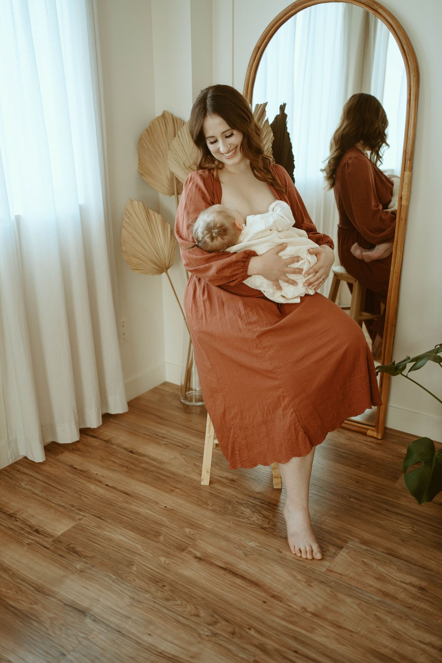 A peaceful moment in a sunlit room shows mother and baby sitting near a decorative mirror.