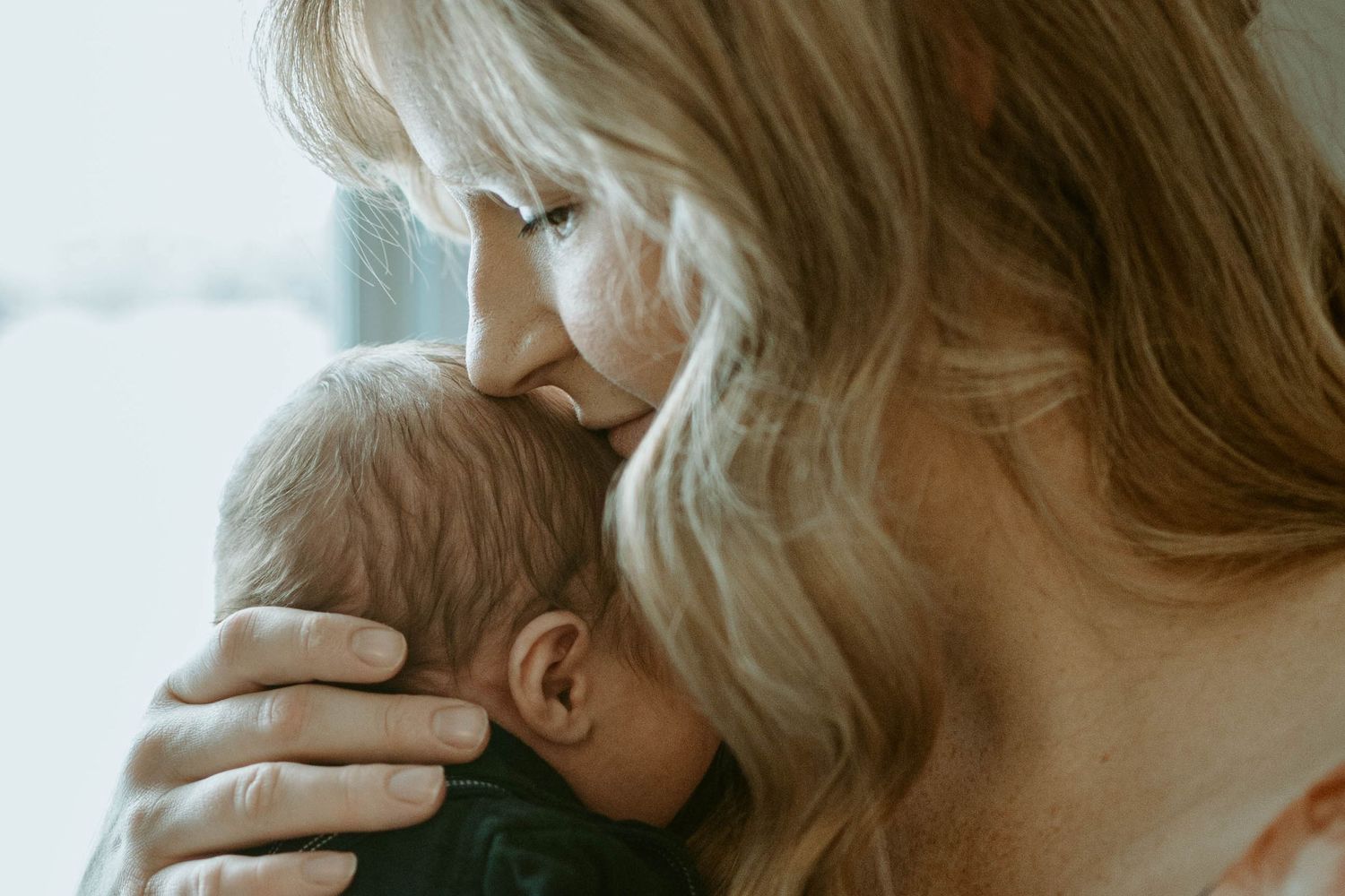 An intimate maternal moment captured in soft window light.