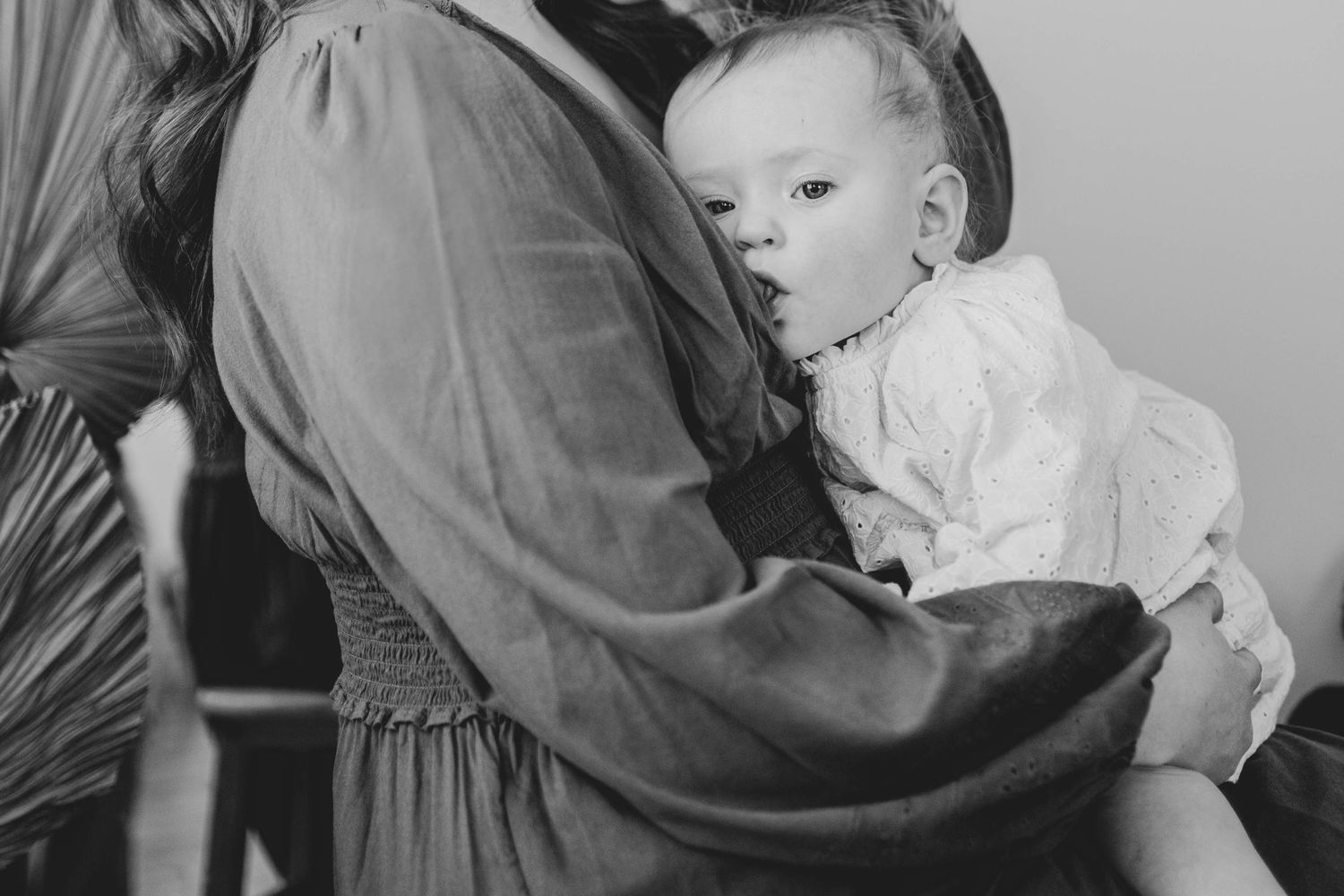 Intimate black and white portrait of an infant being held in soft natural light.