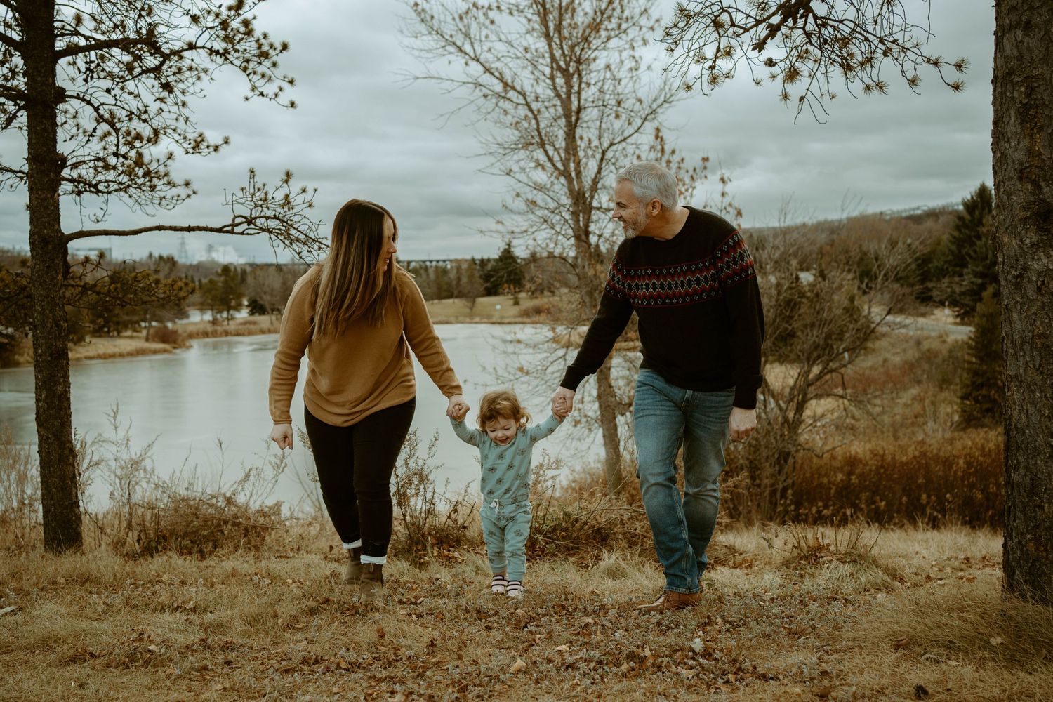 A family walks hand in hand through an autumn landscape with a lake in the background.