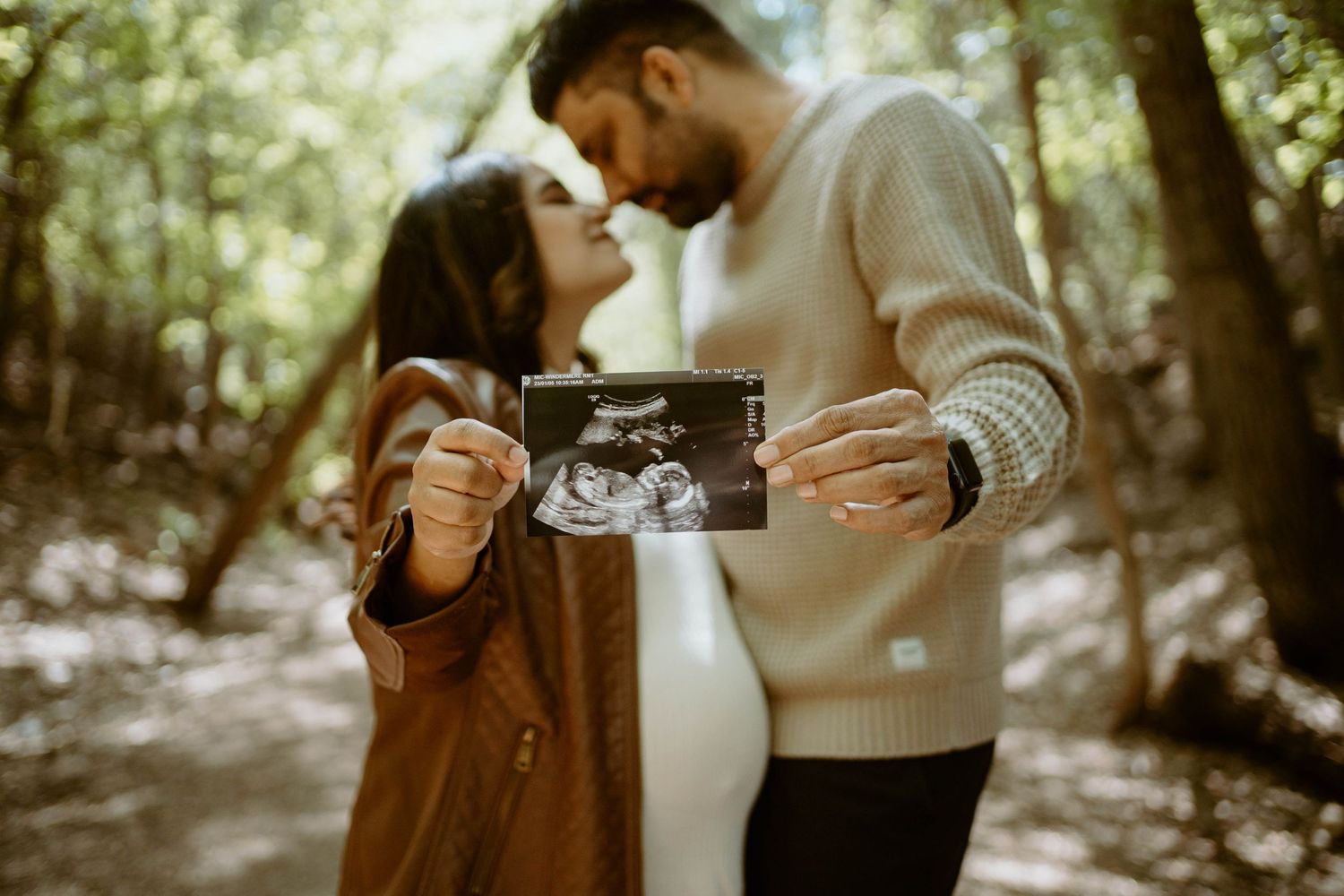 A romantic outdoor forest scene with a couple holding an ultrasound photo for a maternity session.