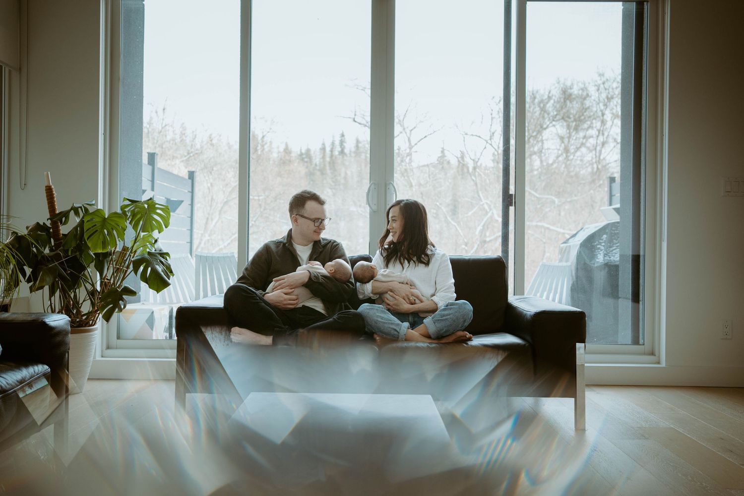 Family resting on couch against large windows with winter landscape visible outside.