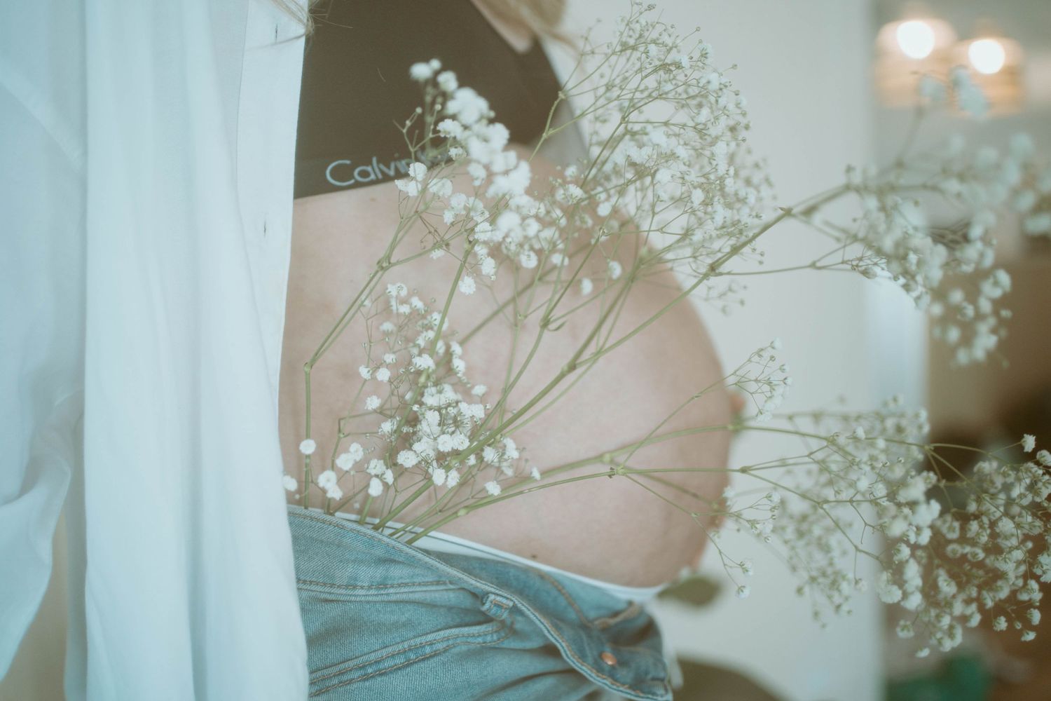 A delicate maternity photo with baby's breath flowers against a pregnant belly in soft lighting.