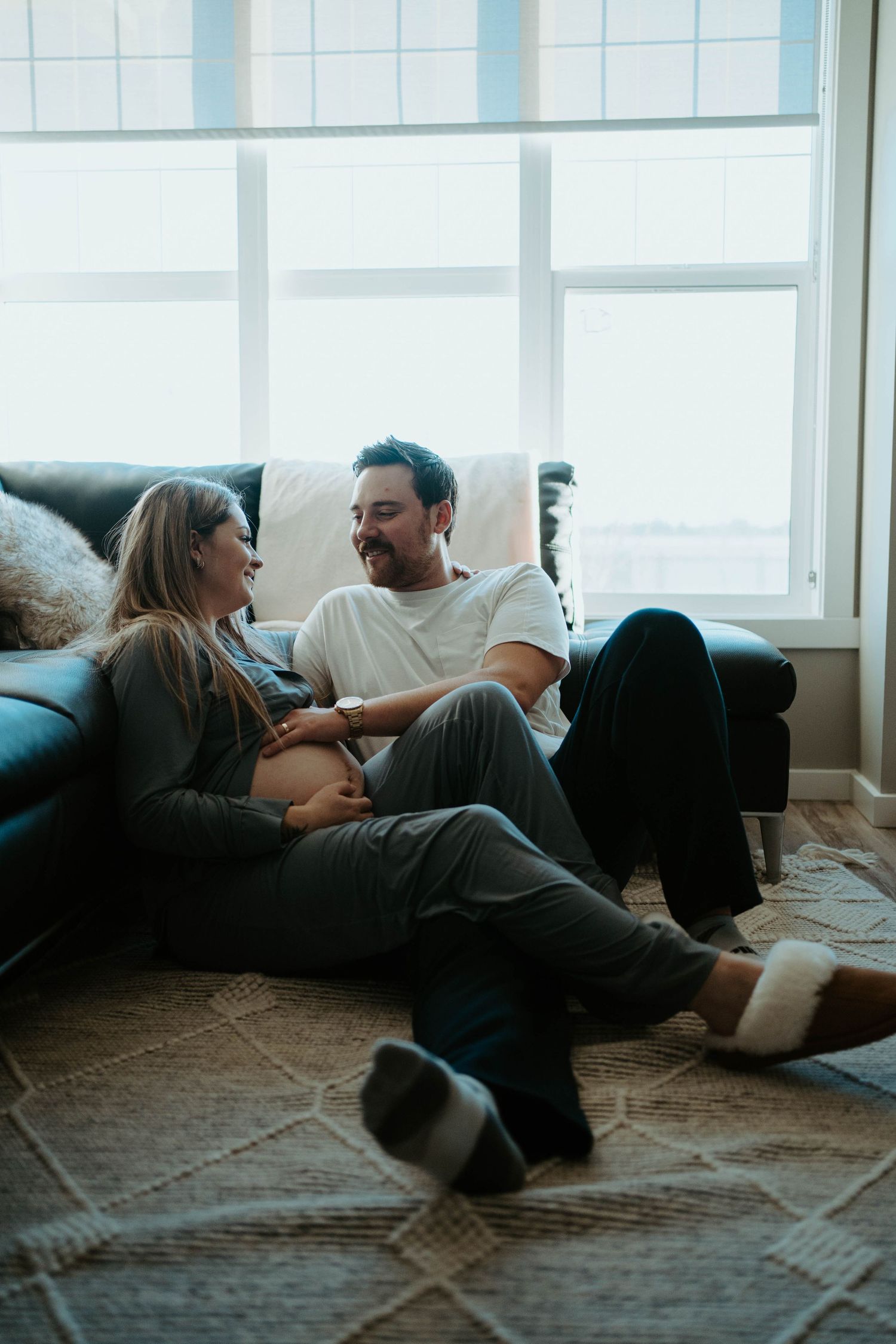 Couple relaxing on floor by window sharing intimate moment during pregnancy.