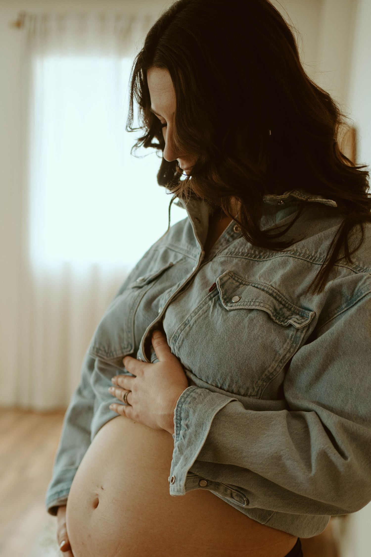 Artistic maternity photo showing a pregnant belly with a light denim jacket in a warm, natural setting.