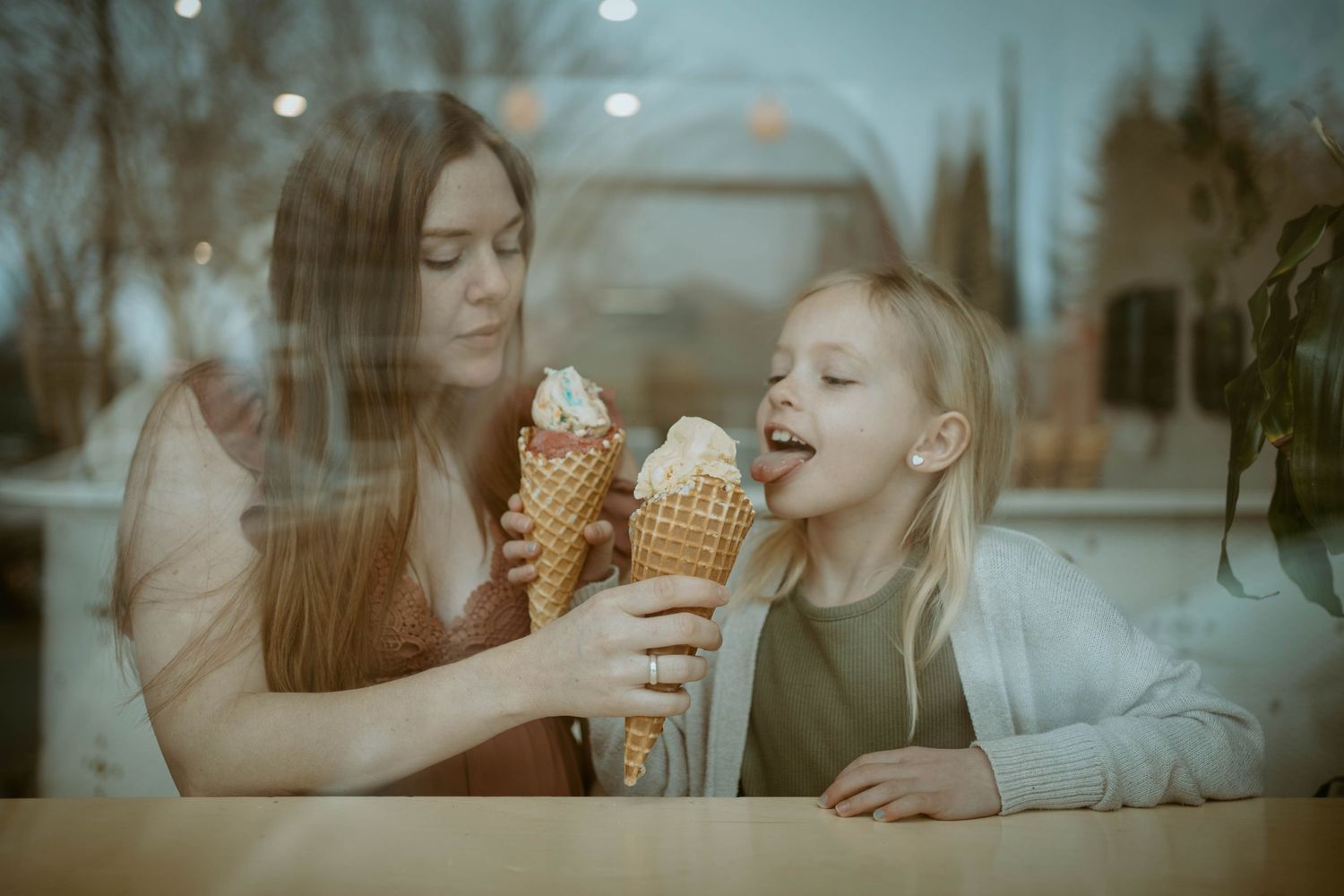 Two people enjoying ice cream cones together at counter with window reflection.