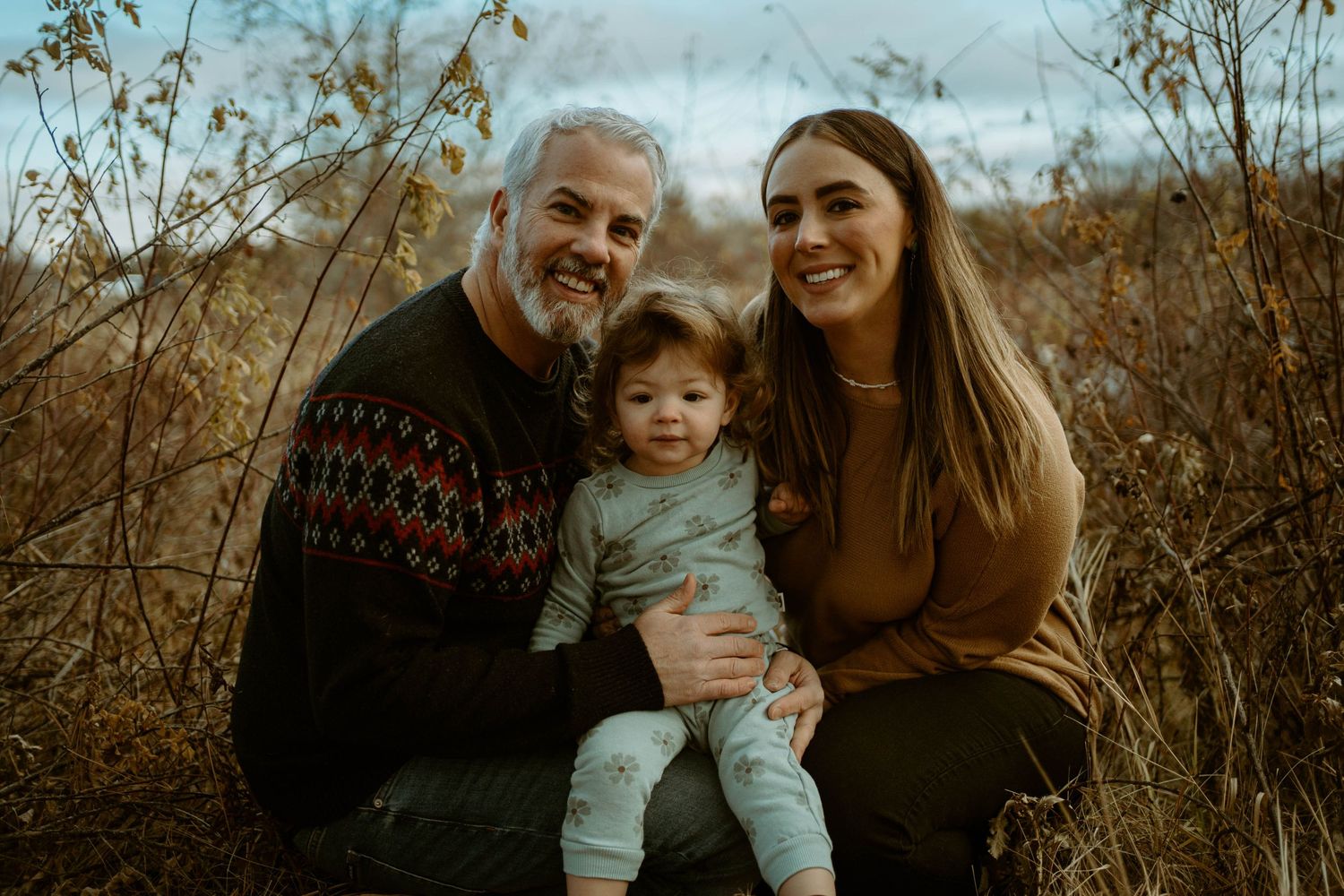 A family enjoys a warm autumn moment together in tall grass during golden hour.