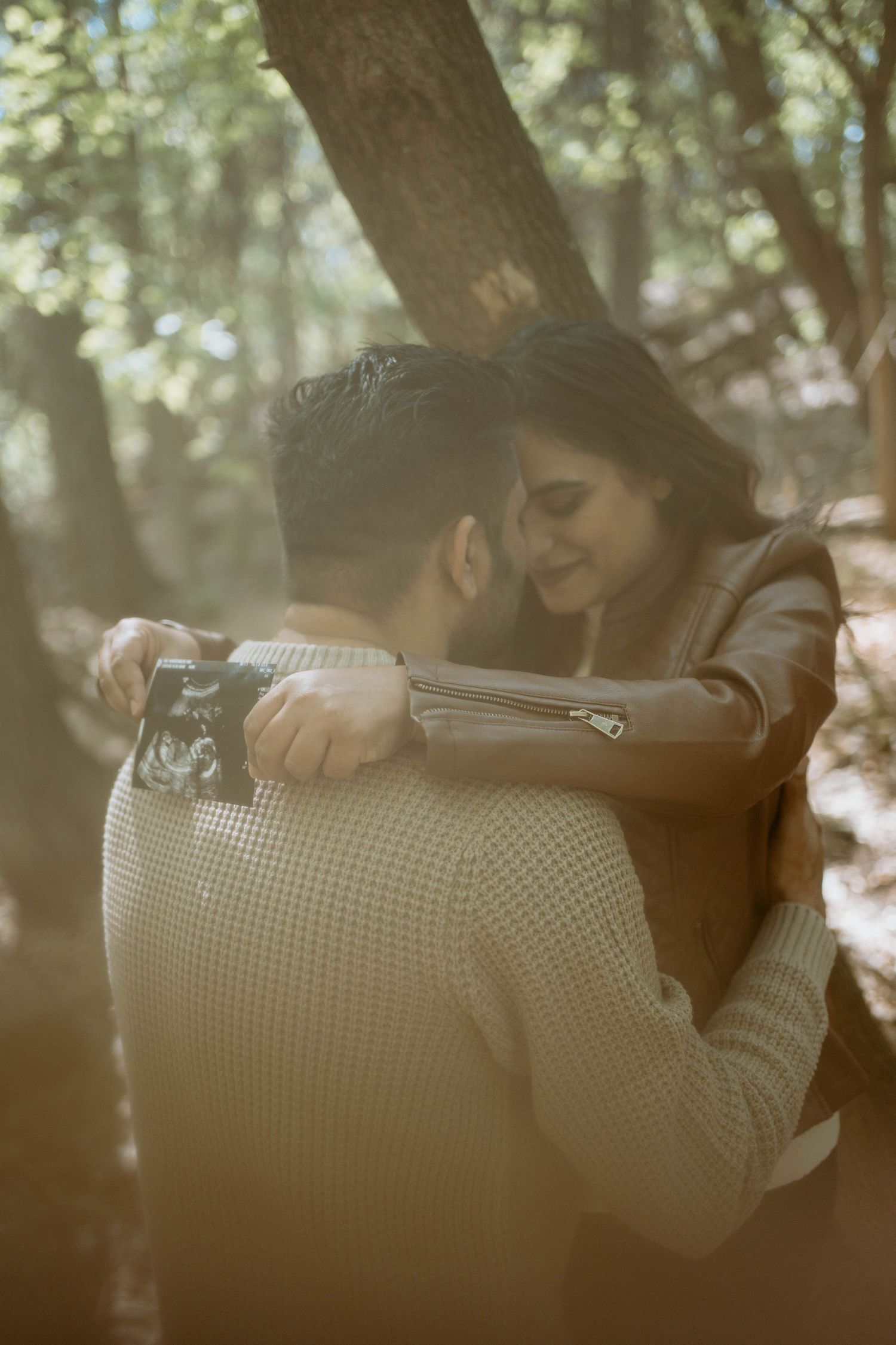 A tender embracing moment captured in a sunlit forest setting.