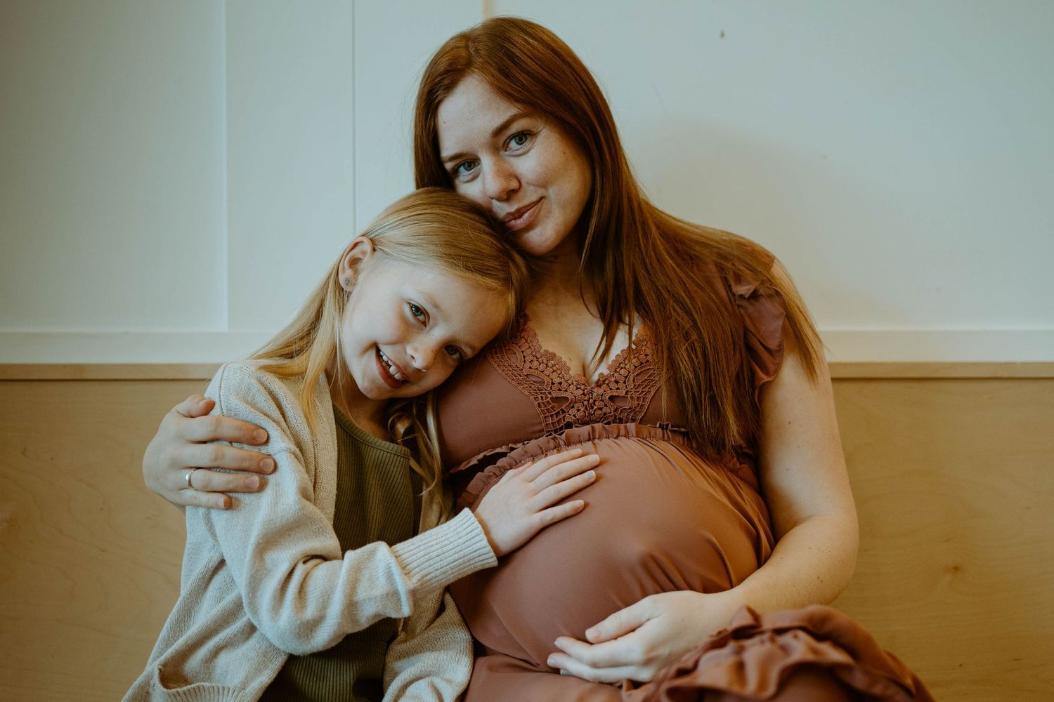 Tender maternity moment captured in warm tones with natural window light.