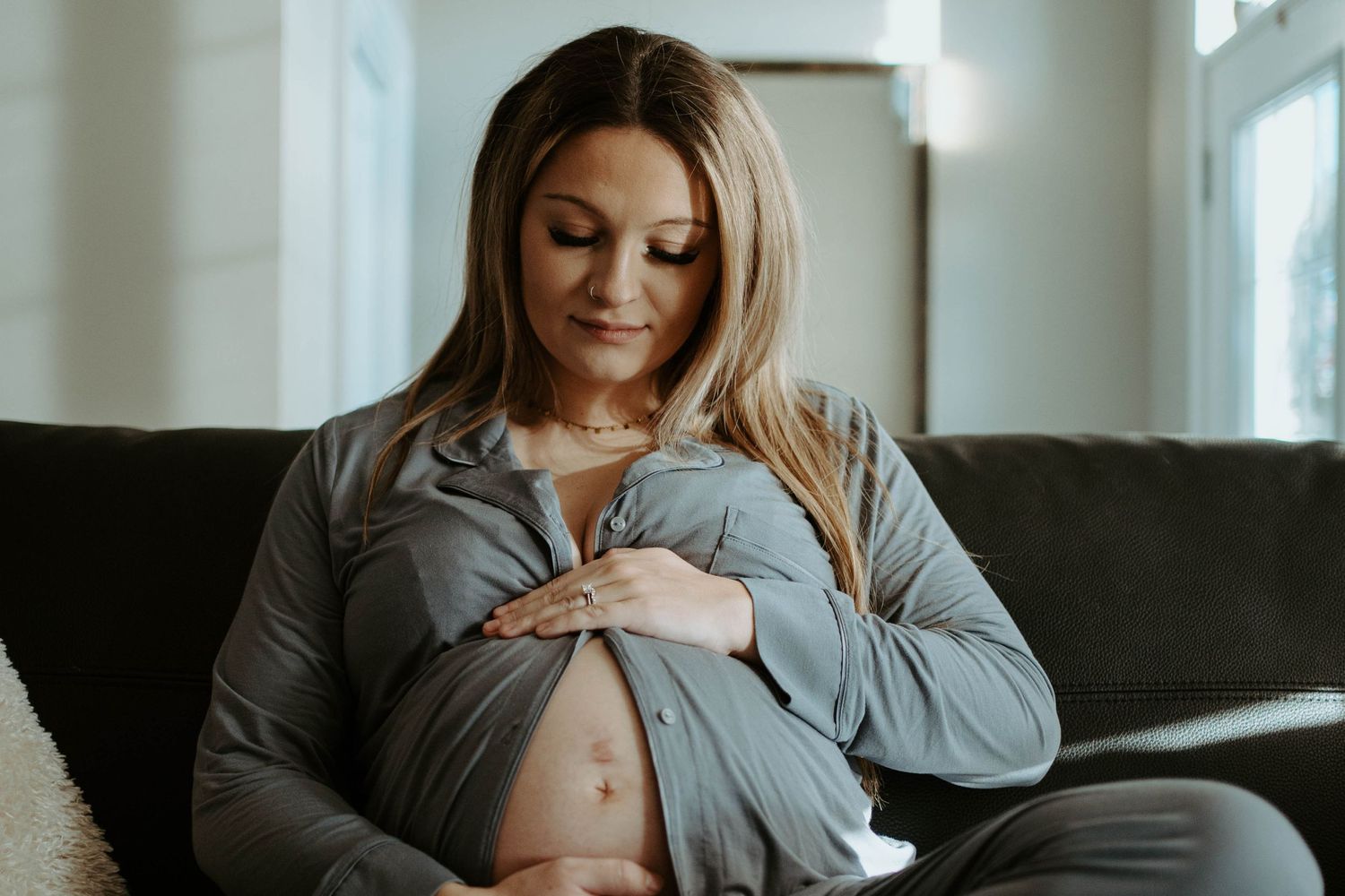Expectant mother in grey sweater sitting on couch touching her pregnant belly.