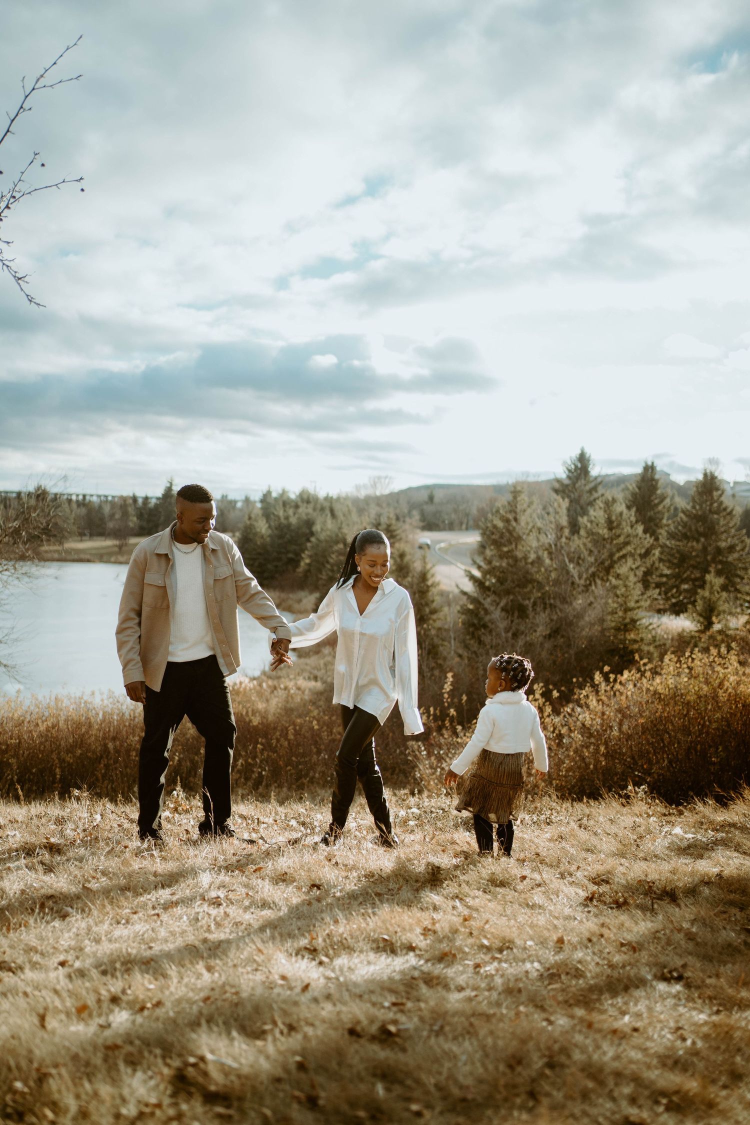 Three people walk together on a hilltop path with a scenic lake view in the background.