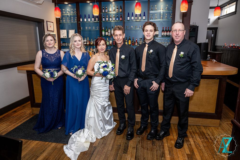 Wedding party in formal attire poses together at a bar with blue lighting and wooden decor.