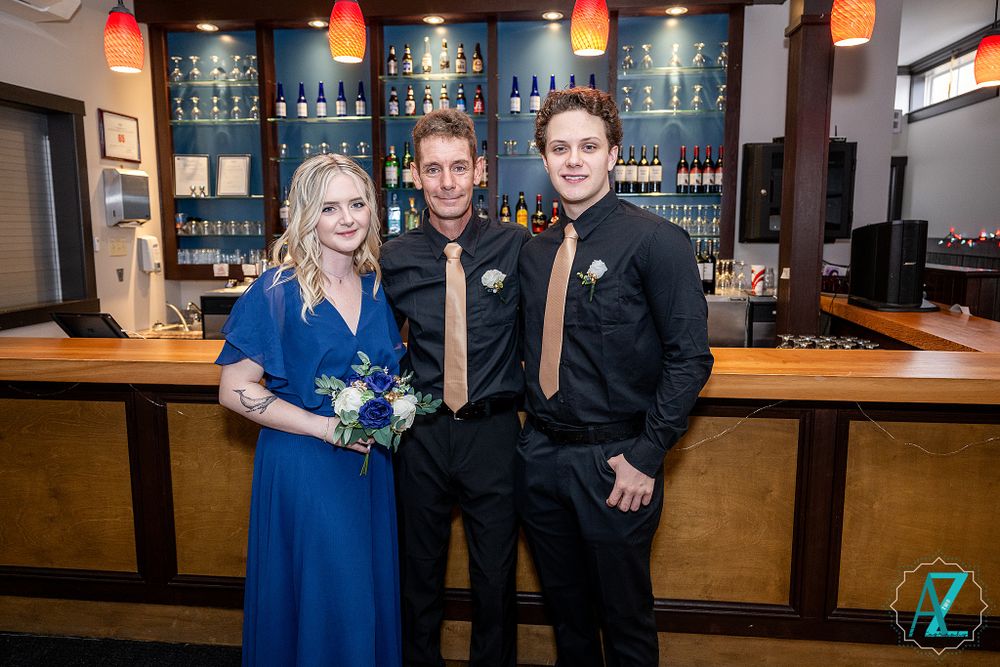 Wedding party members pose in formal attire at bar with blue lighting and pendant lamps.