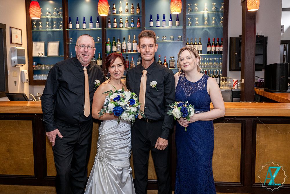 Small wedding group poses at elegant bar with blue backlighting and wooden counter.