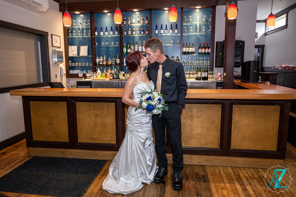 Wedding couple embraces at elegant bar with wooden counter and blue backlit shelving.